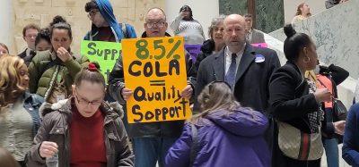 Man at Albany Rally holding up a yellow sign that says 8.5% Cola Quality Support